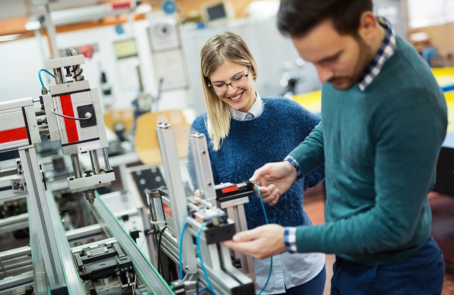 Two people working in a factory with some machines