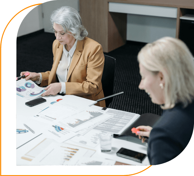 Two women sitting at a table with papers and pens.