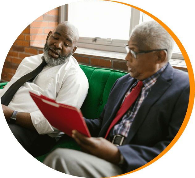 Two men sitting on a couch looking at papers.