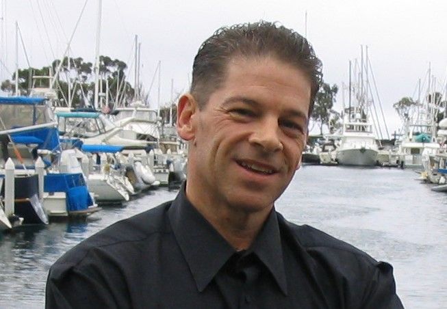 A man in black shirt standing next to boats.