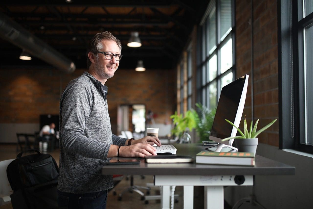 A man standing at his desk with a laptop.